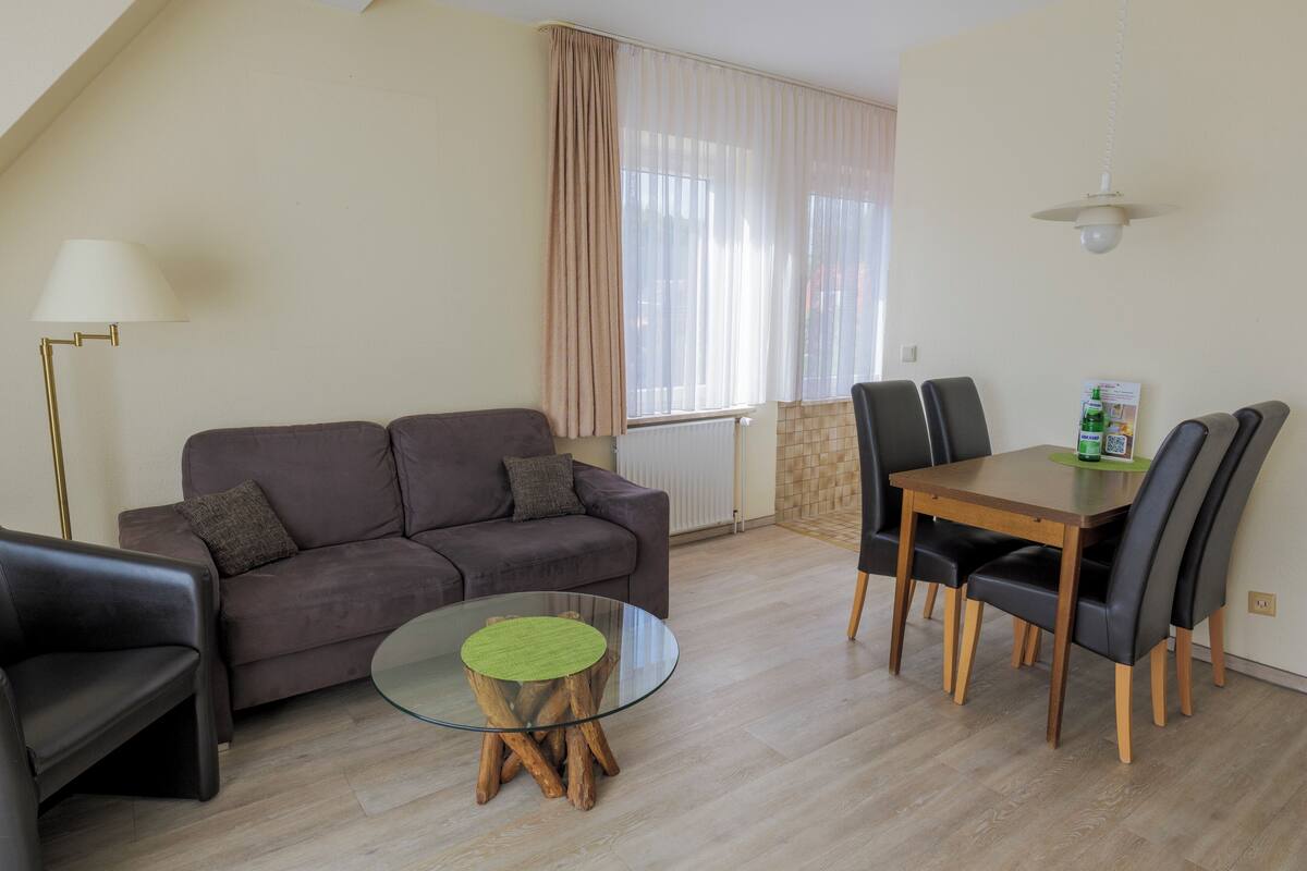 A modern living room with a sofa, a glass coffee table, a dining table with chairs, and a lamp.