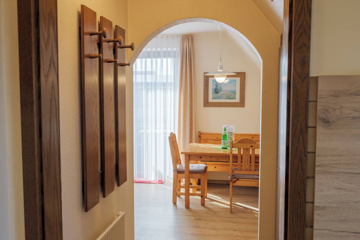 A hallway leading to a dining area with wooden furniture and a painting on the wall.