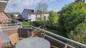 A balcony with wicker chairs and a table, overlooking a garden and neighboring houses. - Appartementhaus Alt Büsum (Büsum)