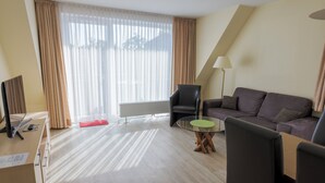 A modern hotel room with a sofa, a round glass table, a chair, a desk with a computer, and a lamp. - Appartementhaus Alt Büsum (Büsum)