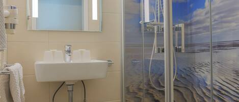 A bathroom with a glass-enclosed shower, a sink with a mirror above it, and a toilet.