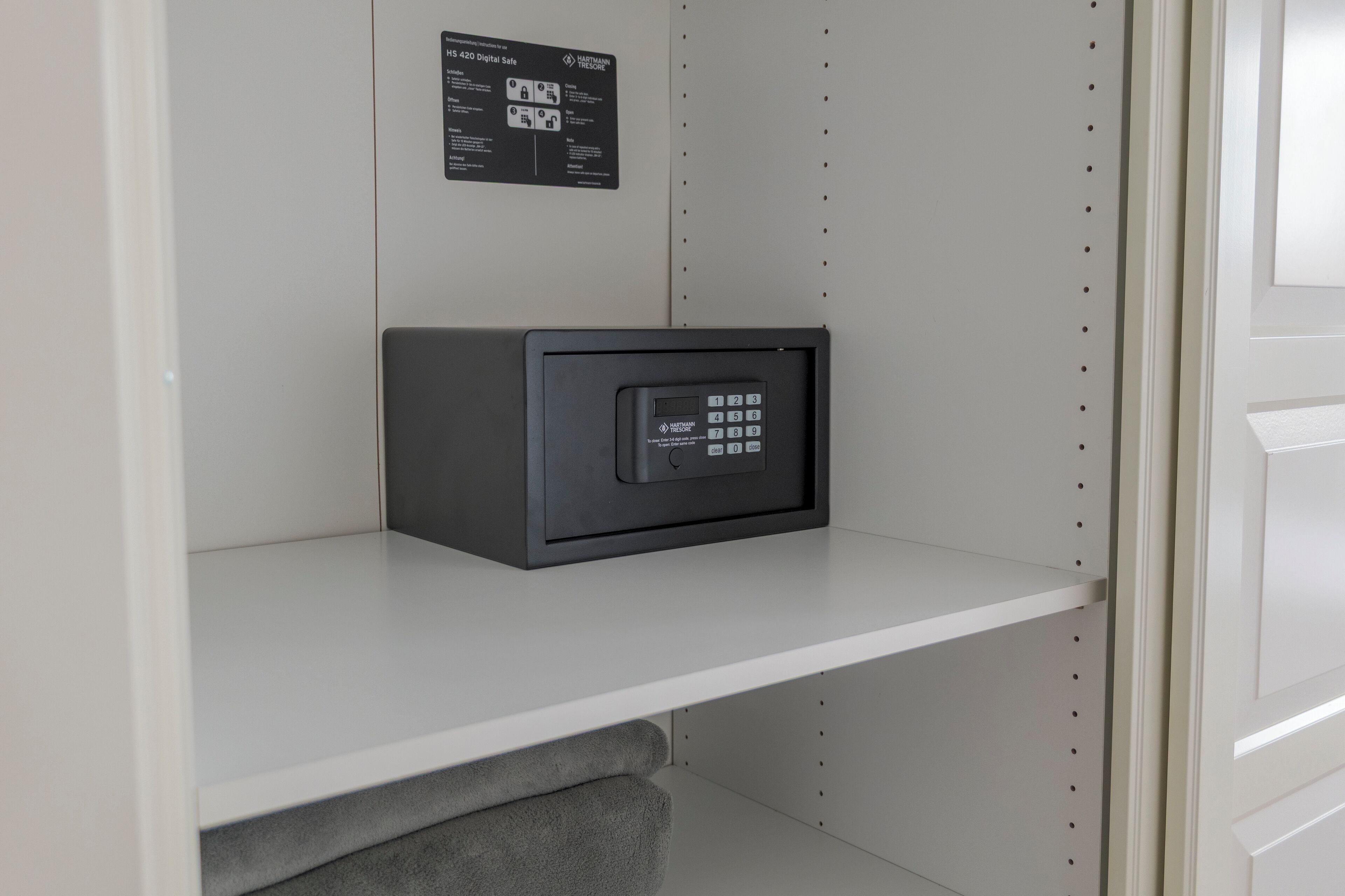 A secure storage unit with a keypad on a white shelf in a room with a white door and wall.