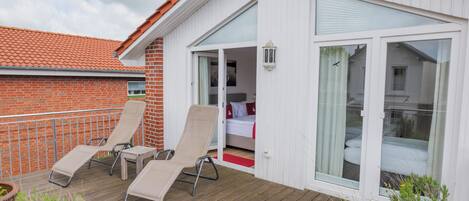 A balcony with two lounge chairs, a wooden deck, and a potted plant.