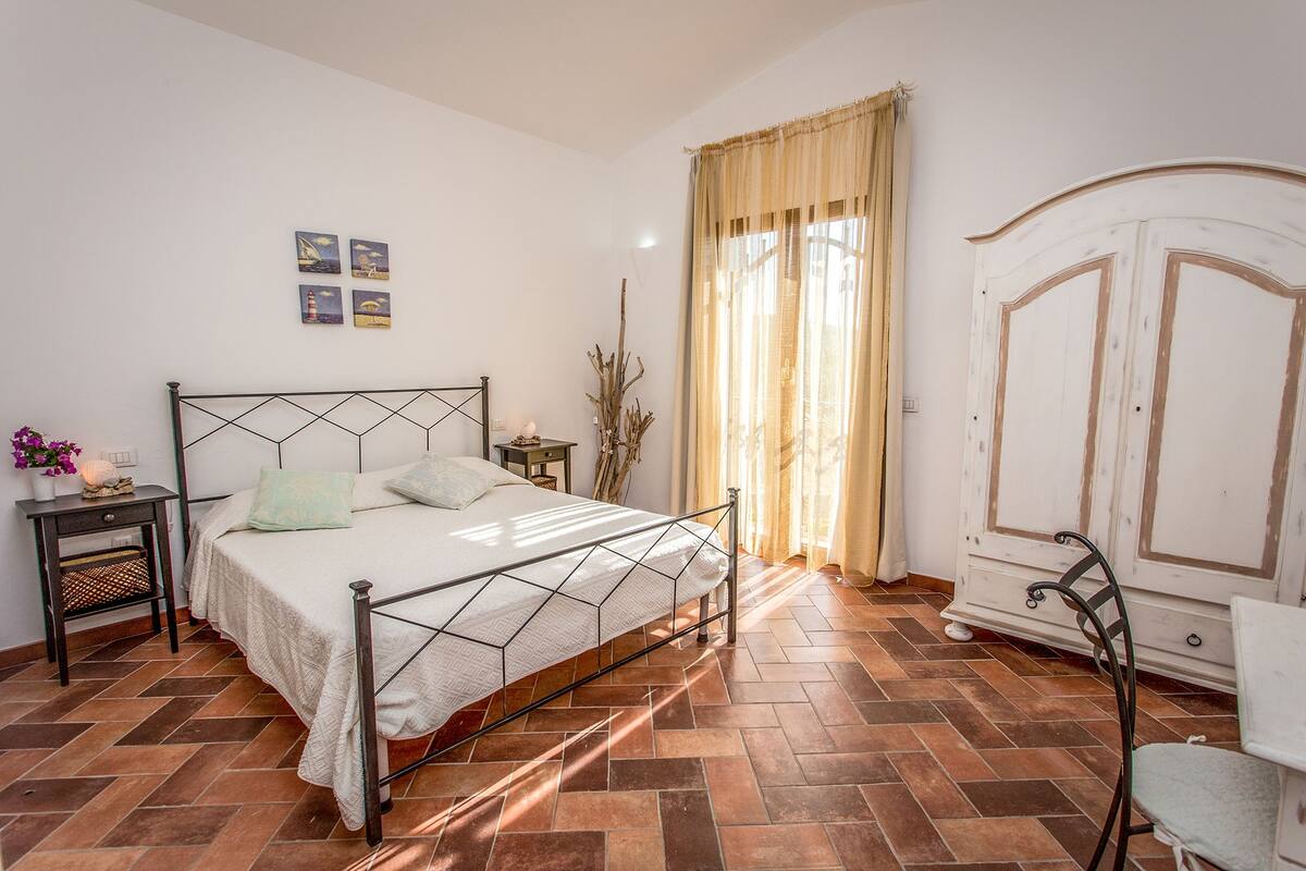 A bedroom with a metal bed frame, a nightstand, a dresser, and a window with curtains.