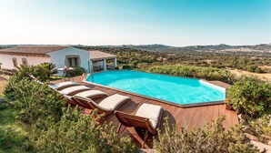 Ein Pool mit Liegestühlen, umgeben von Grün und Blick auf ferne Hügel.