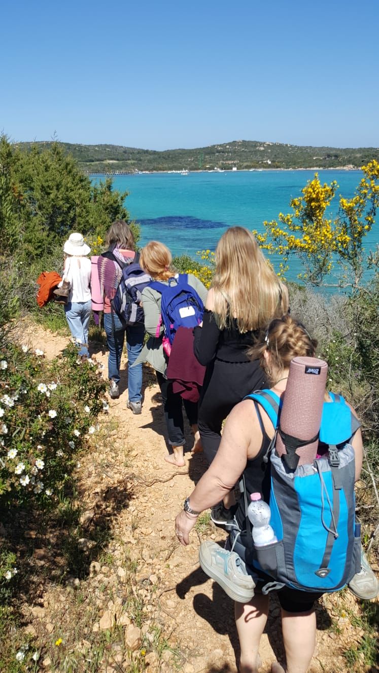 A group of people walking on a dirt path with a clear view of the sea and hills in the background.