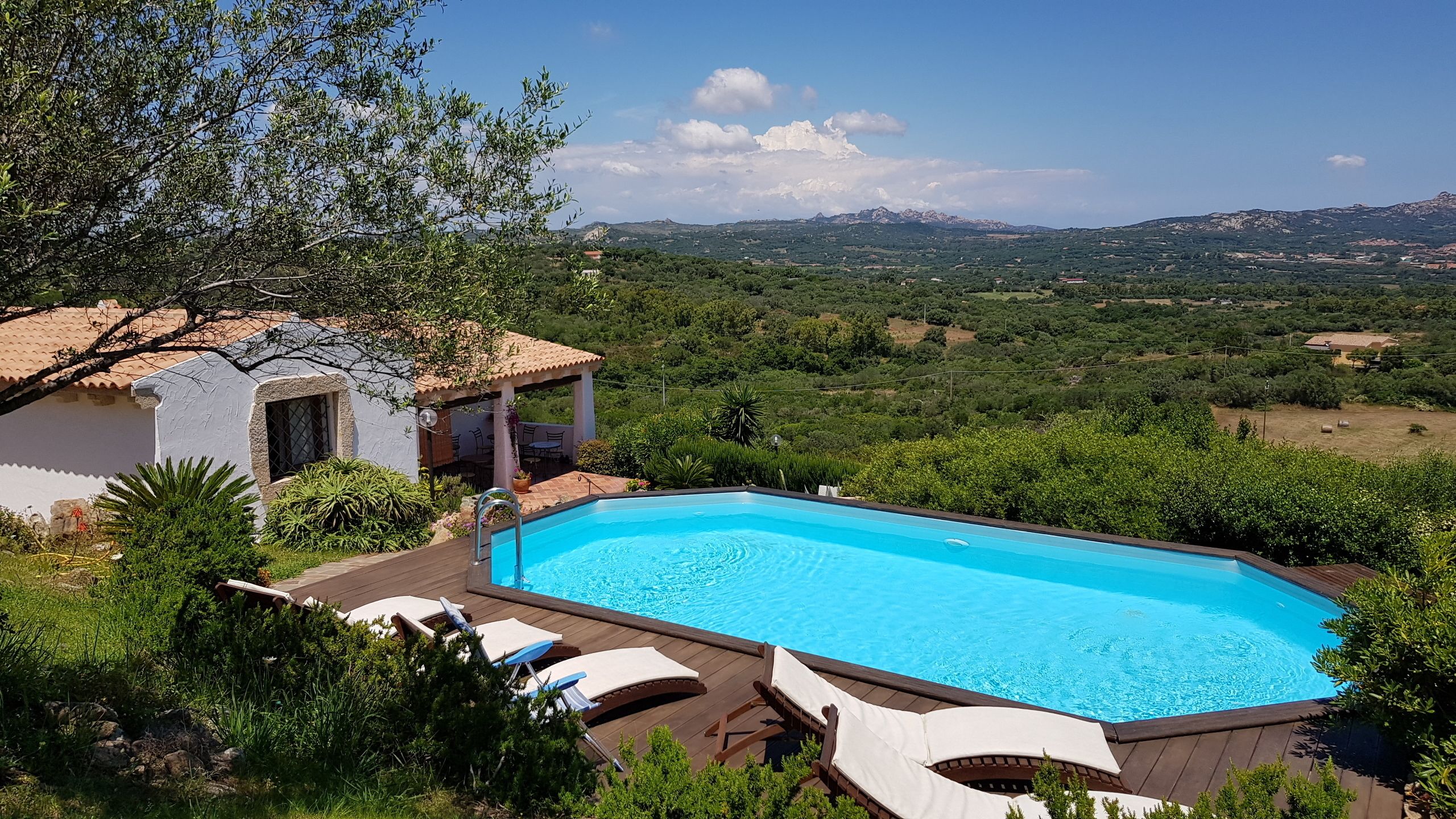 Una piscina con sillas de descanso, rodeada de vegetación y con vistas a montañas lejanas.