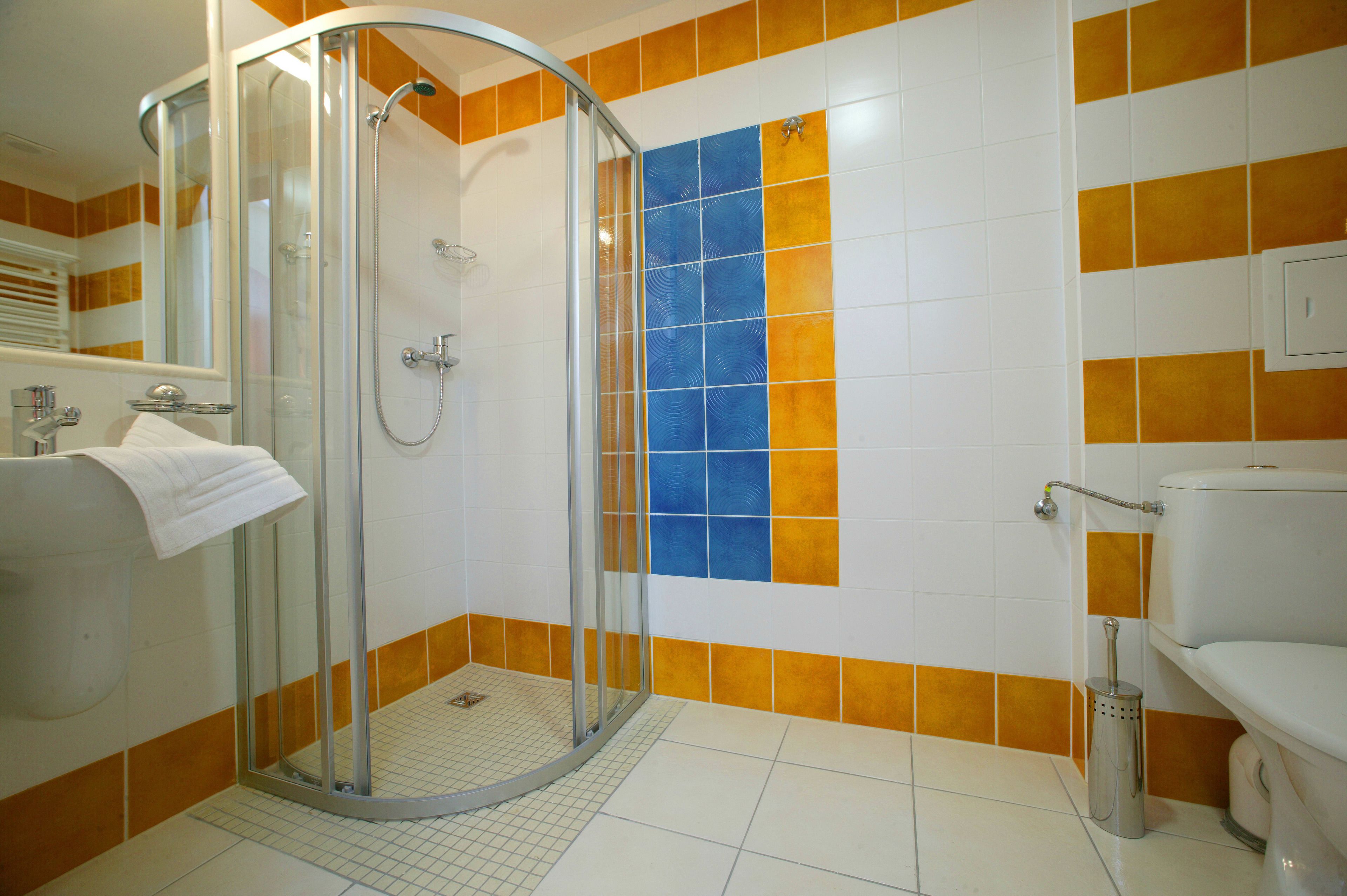 Ein Badezimmer mit einer gläsernen Duschkabine, orange-weißen Fliesen an den Wänden, einer weißen Toilette und einem Handtrockner.
