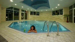 An indoor swimming pool with a tiled floor, a person resting by the pool, and a ceiling with recessed lighting. - Hotel Gold (Swinoujscie)