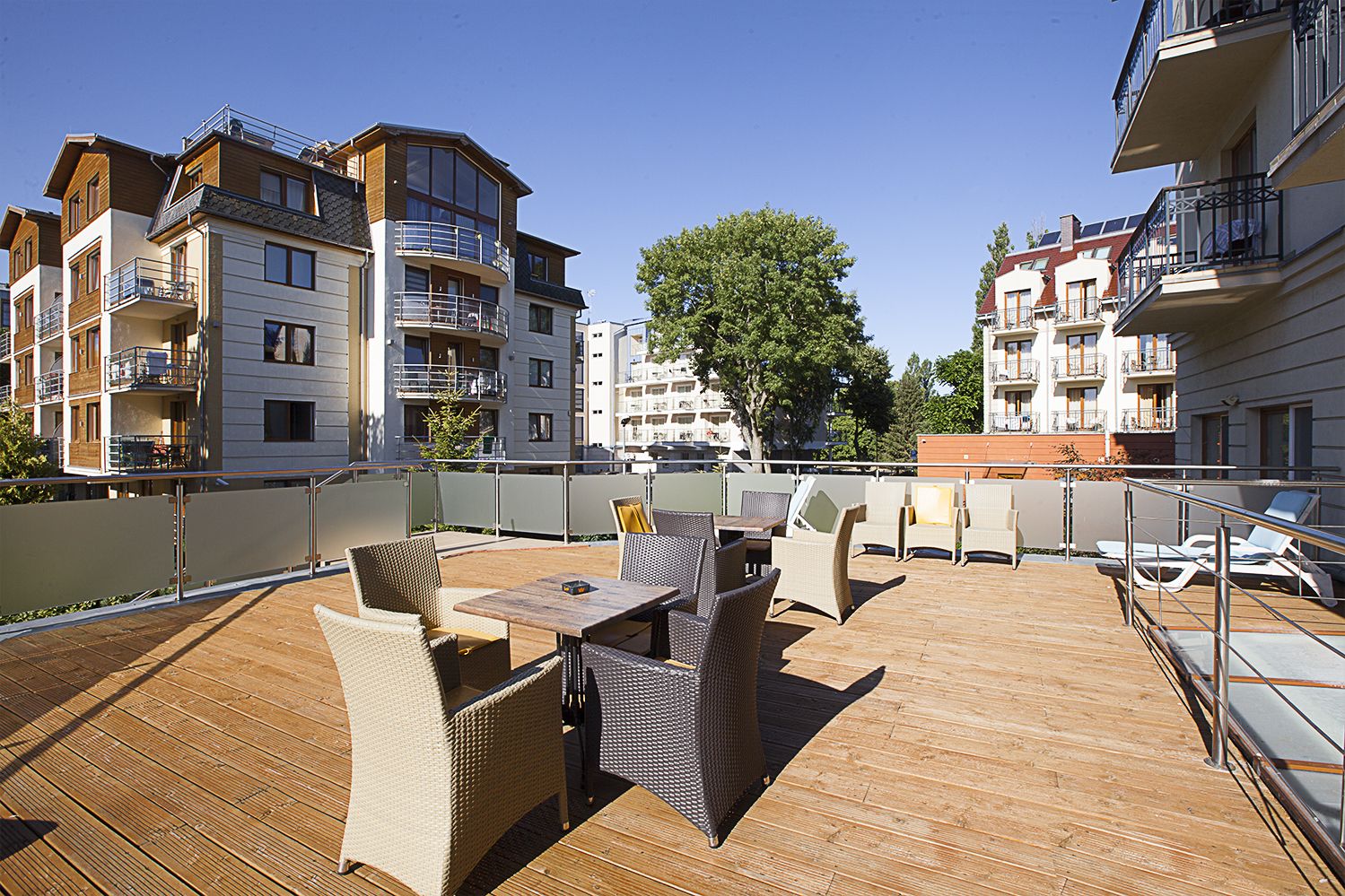 A rooftop terrace with outdoor furniture, a view of surrounding buildings, and a clear sky.