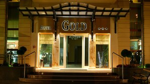 A hotel entrance with a prominent 'GOLD' sign, a set of stairs leading up to the doors, and a bench outside. - Hotel Gold (Swinoujscie)