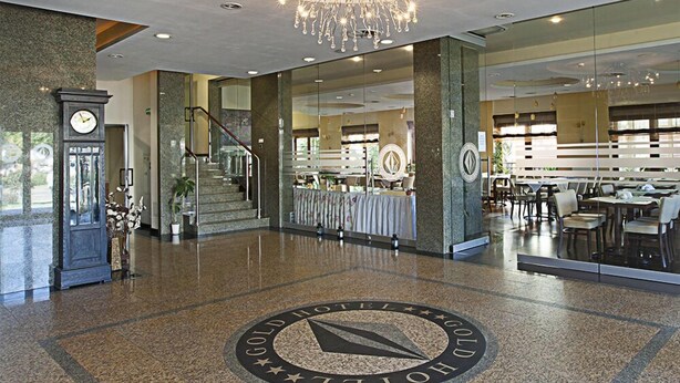 A spacious lobby with a grand chandelier, a clock, and a circular emblem on the floor. - Hotel Gold (Swinoujscie)
