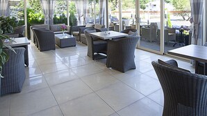 A spacious indoor area with large windows, wicker furniture, and a chandelier. - Hotel Gold (Swinoujscie)