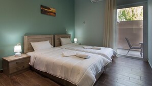 Een slaapkamer met twee bedden, een nachtkastje met een lamp, een schilderij aan de muur en uitzicht op de omgeving via een schuifdeur.
