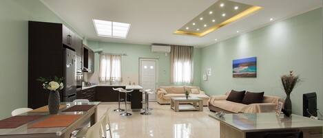 A modern living room with a dining area, kitchen, and a large window with curtains.