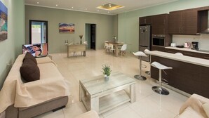 Een moderne woonkamer met een bank, een salontafel en een eetgedeelte met een tafel en stoelen. Er is een keuken met kasten en apparatuur.
