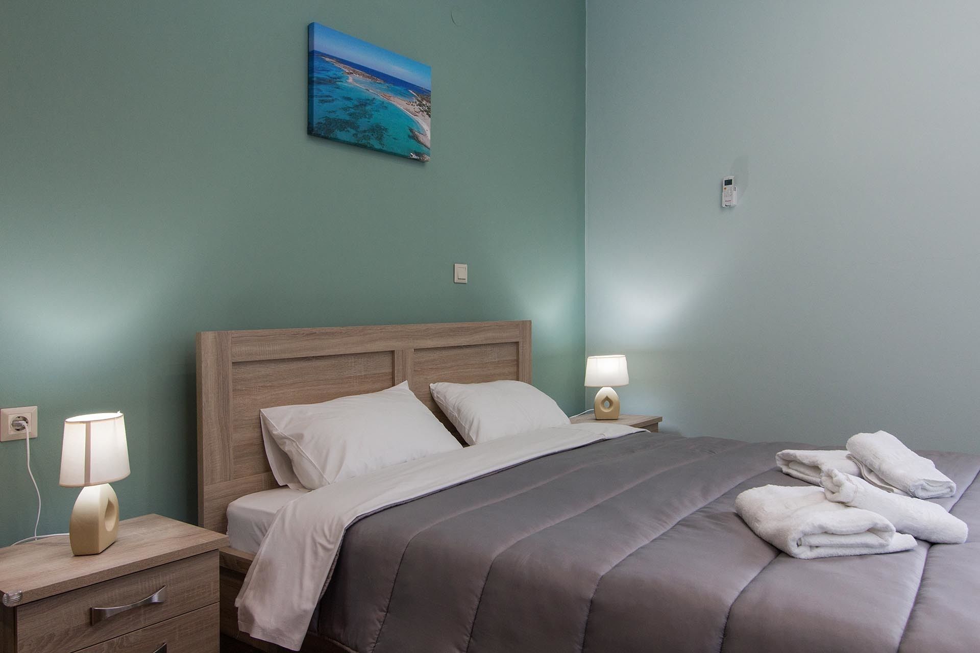Un dormitorio con cama, mesitas de noche, lámpara y un cuadro en la pared.