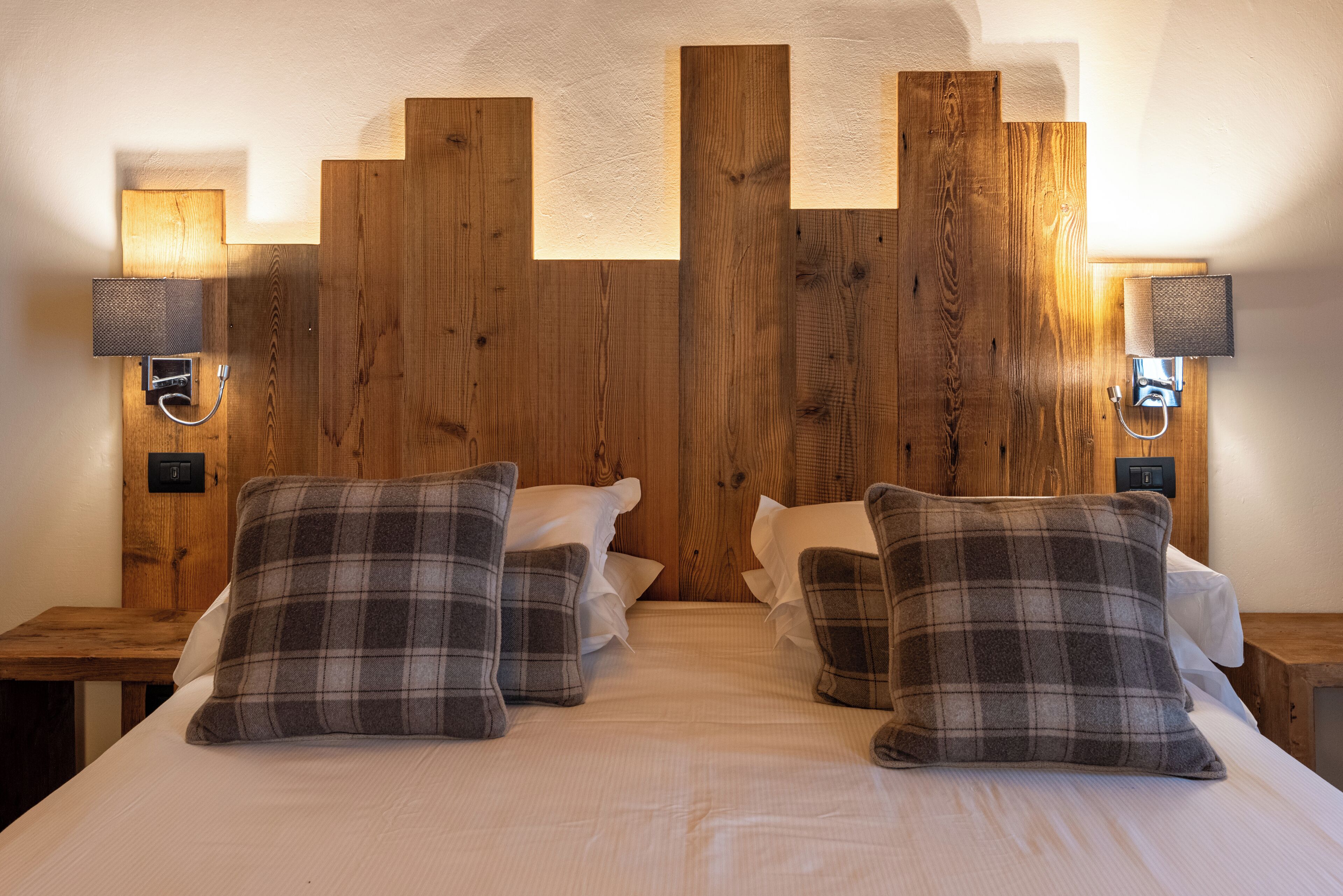 Un dormitorio con cabecera de madera, dos mesitas de noche y almohadas a cuadros.