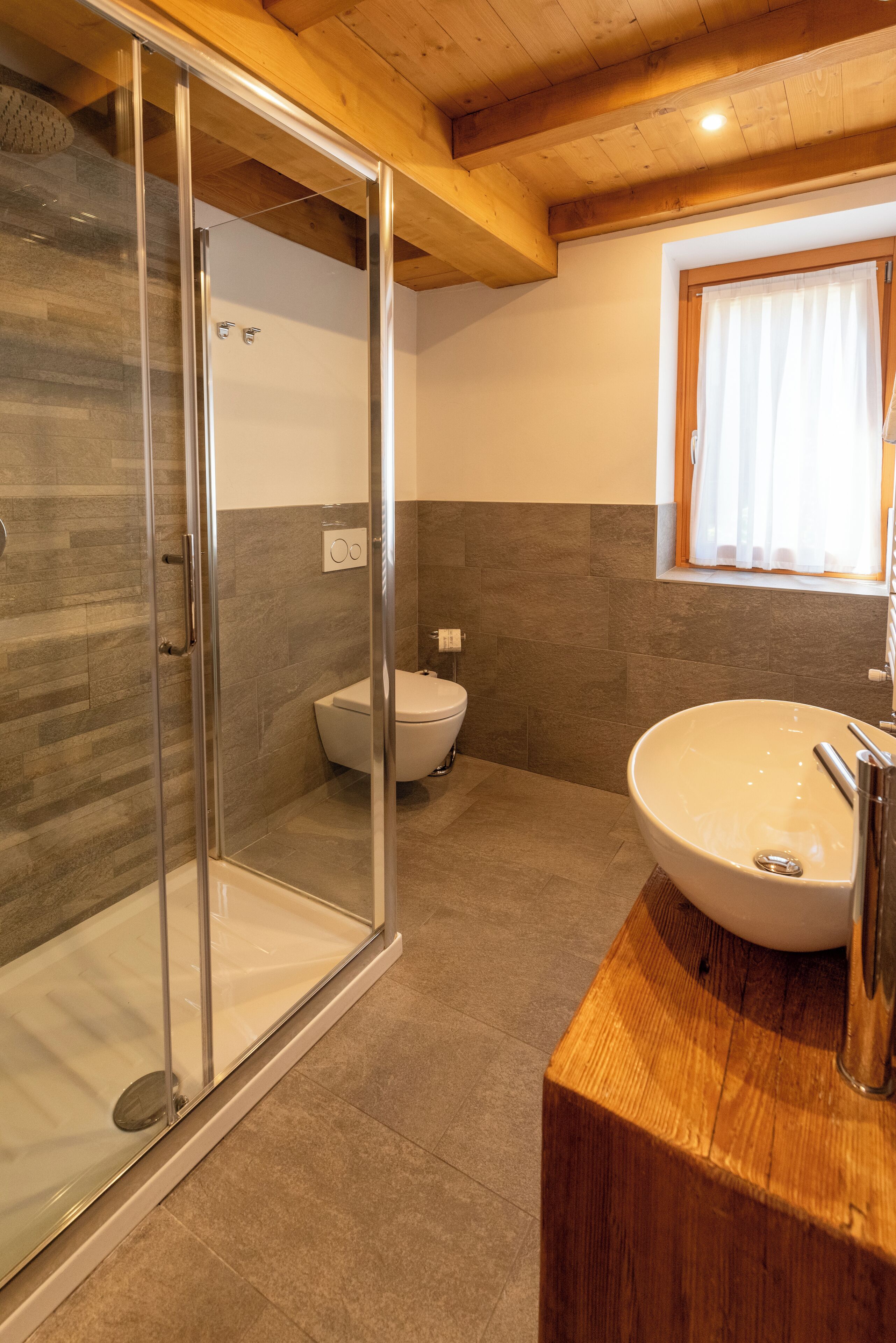 A modern bathroom with a glass shower enclosure, a white toilet, and a wooden vanity with a large sink.