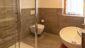 A modern bathroom with a glass shower enclosure, a white toilet, and a wooden vanity with a large sink.