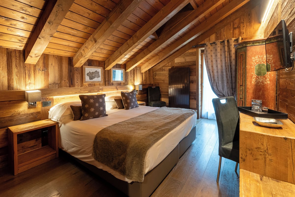 A cozy wooden cabin bedroom with a large bed, a desk, and a chair.