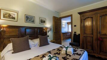 A hotel room with a large bed, wooden headboard, and a wardrobe. There are framed pictures on the wall and a bathroom visible through an open door.