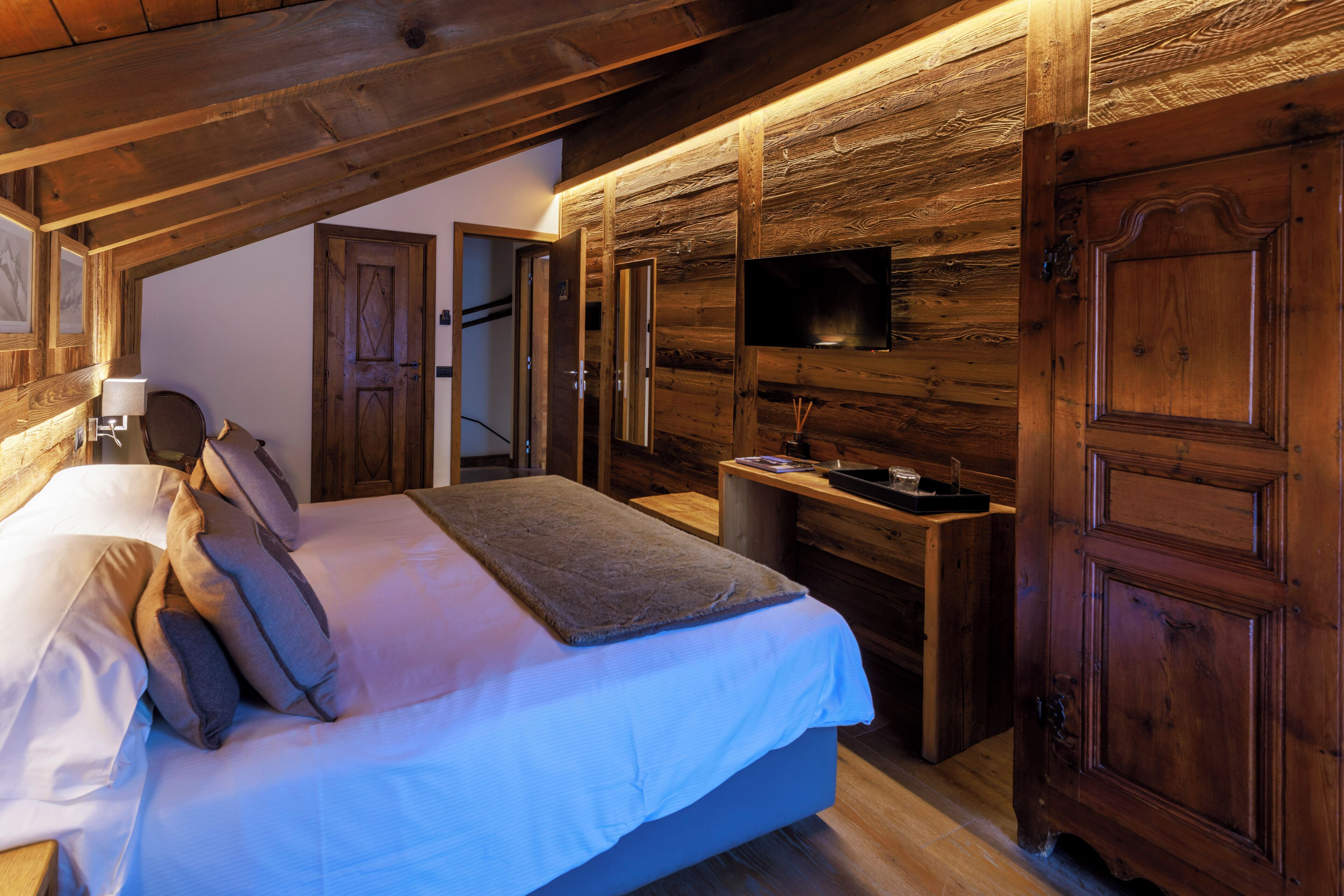 Un dormitorio con techo de madera, una cama con almohadas, una mesita de noche y un televisor montado en la pared.