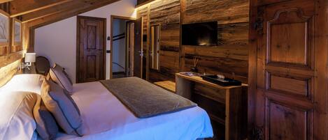 Un dormitorio con techo de madera, una cama con almohadas, una mesita de noche y un televisor montado en la pared.