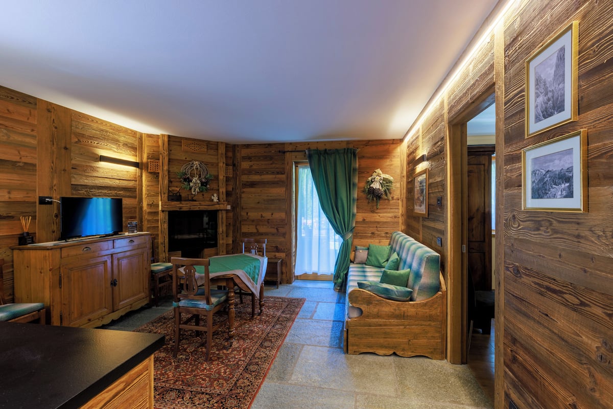 A cozy log cabin interior with a wooden dining area, a sofa, a television, and framed pictures on the walls.