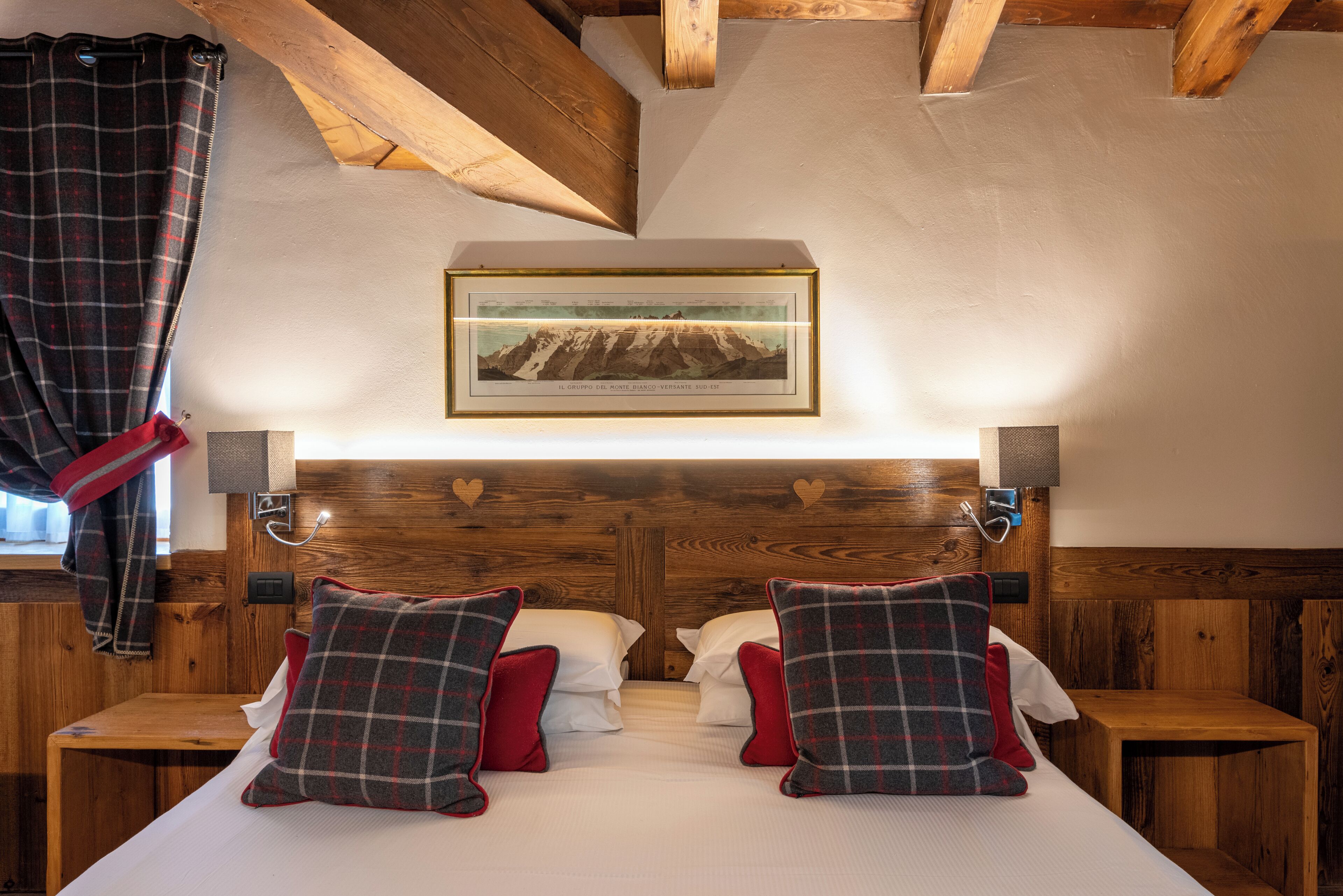A hotel room with a wooden headboard, a framed picture of a mountain, two bedside tables, and plaid-patterned pillows.