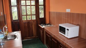 A compact kitchen with a wooden door, a sink, a gas stove, and a white microwave. - Selfcate Luxury Apartments (Kandy)