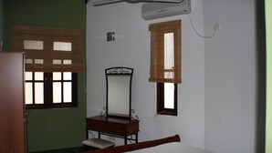 A bedroom with a bed, a wooden dresser, a mirror, and two windows with blinds. - Selfcate Luxury Apartments (Kandy)