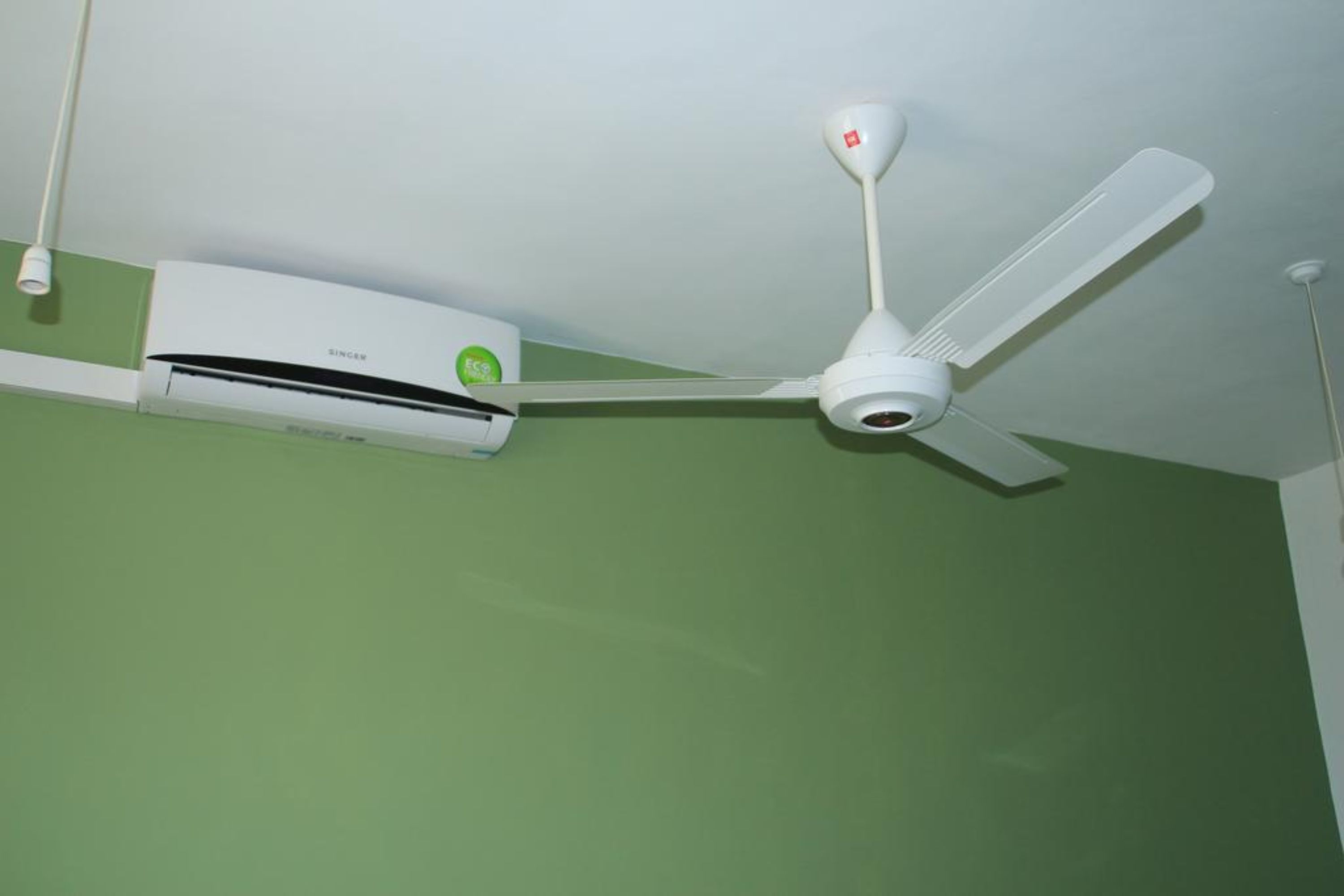 Um ventilador de teto e um aparelho de ar condicionado fixados numa parede verde.