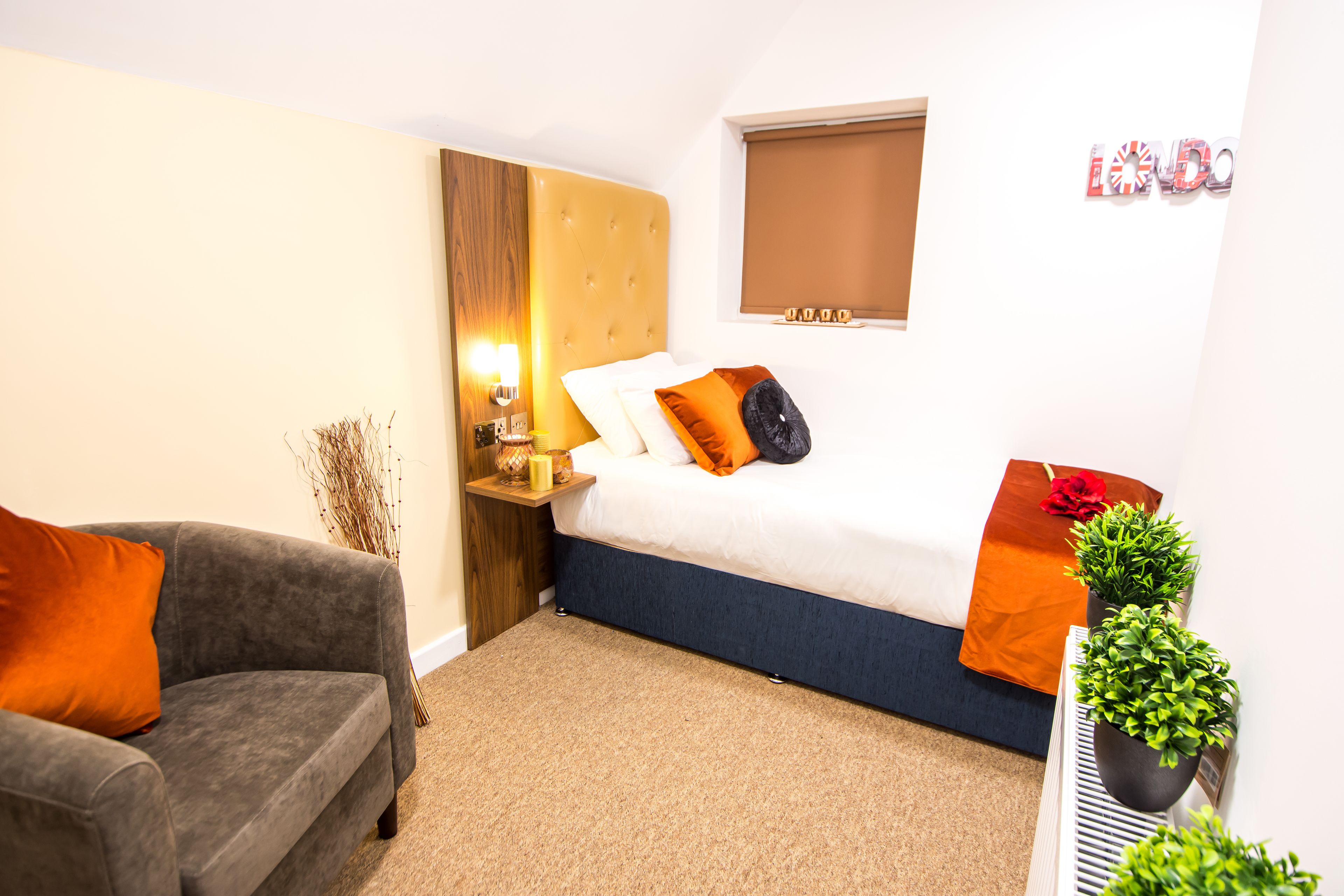 Ein Hotelzimmer mit Bett, Sofa, Nachttisch mit Lampe und einem Fenster mit Jalousien.