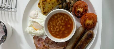 A plate of breakfast food including eggs, beans, sausages, bacon, mushrooms, and grilled tomatoes.