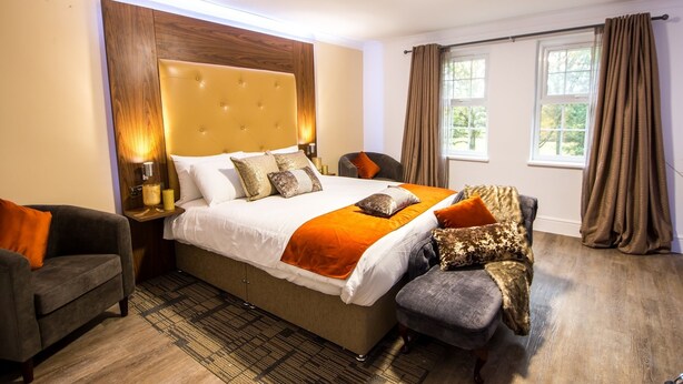 A hotel room with a large bed, a sofa, a nightstand, and a window with curtains. - Trivelles Gatwick (Crawley)