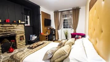 Una camera da letto con camino in pietra, un letto con numerosi cuscini, un comodino in legno, una televisione e una finestra con tende.
