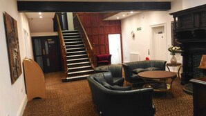 A lobby with a staircase, leather armchairs, a round table, and a fireplace. - Trivelles Gatwick (Crawley)