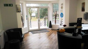 A reception area with a desk, chairs, a fire exit sign, and a view of the outside. - Trivelles Gatwick (Crawley)