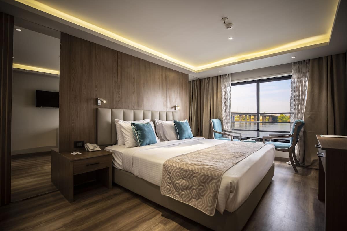 Habitación de hotel moderna con una cama grande, un escritorio y una silla. Se ve una ventana con vistas a la ciudad.