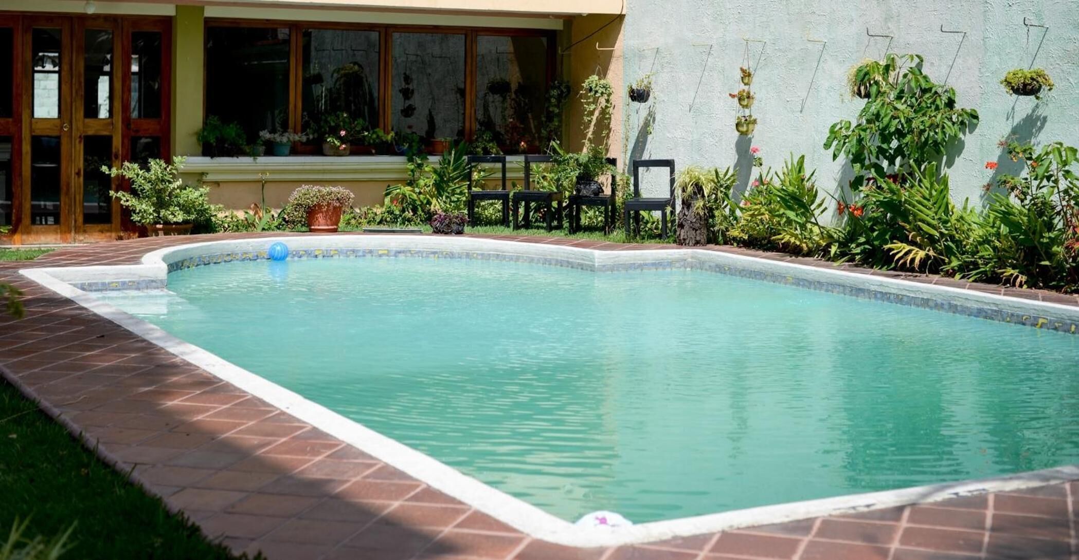 Una piscina rectangular con borde de azulejos, rodeada por un patio de ladrillo.