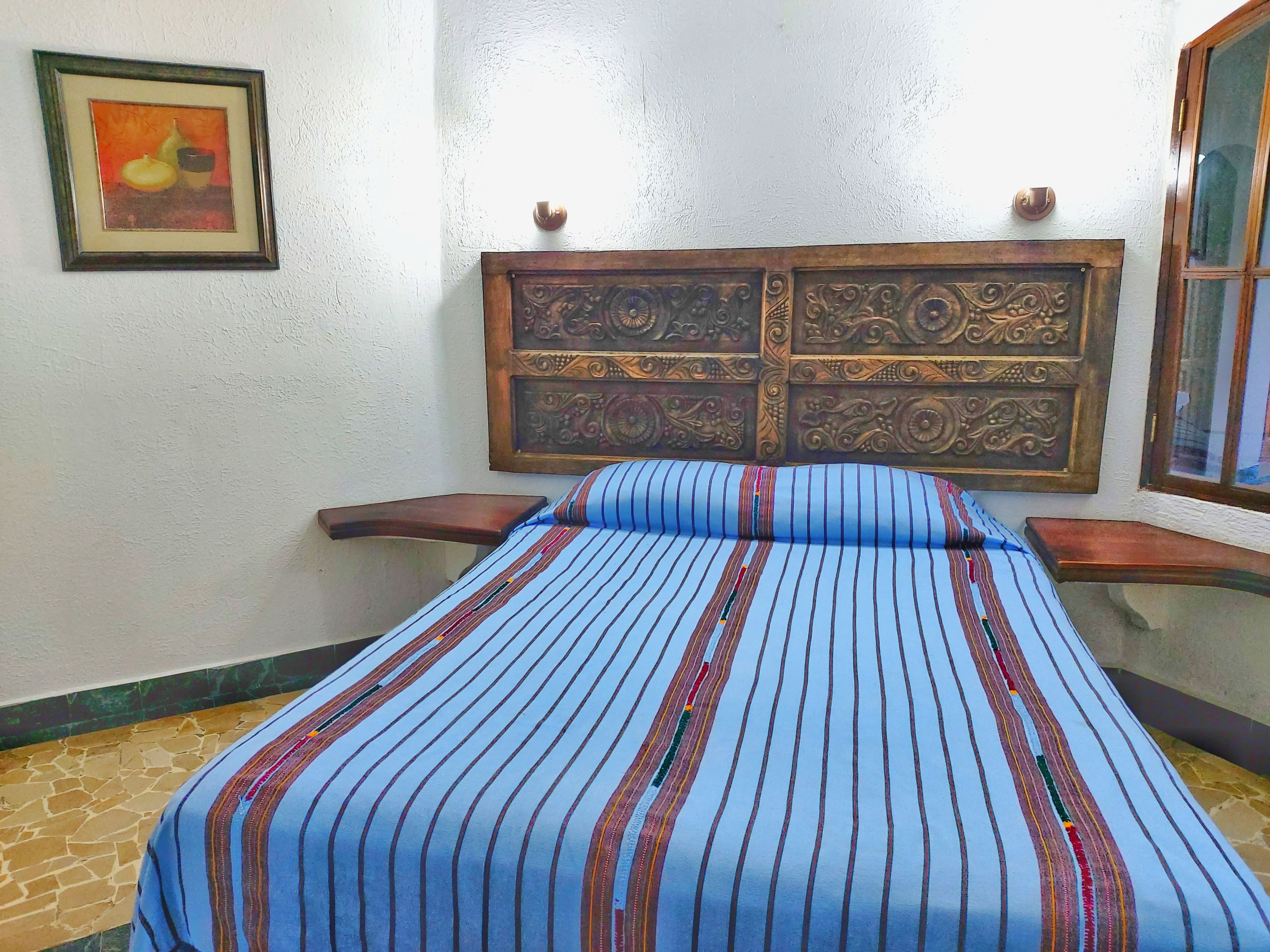 A room with a bed, a framed picture on the wall, and a decorative headboard.
