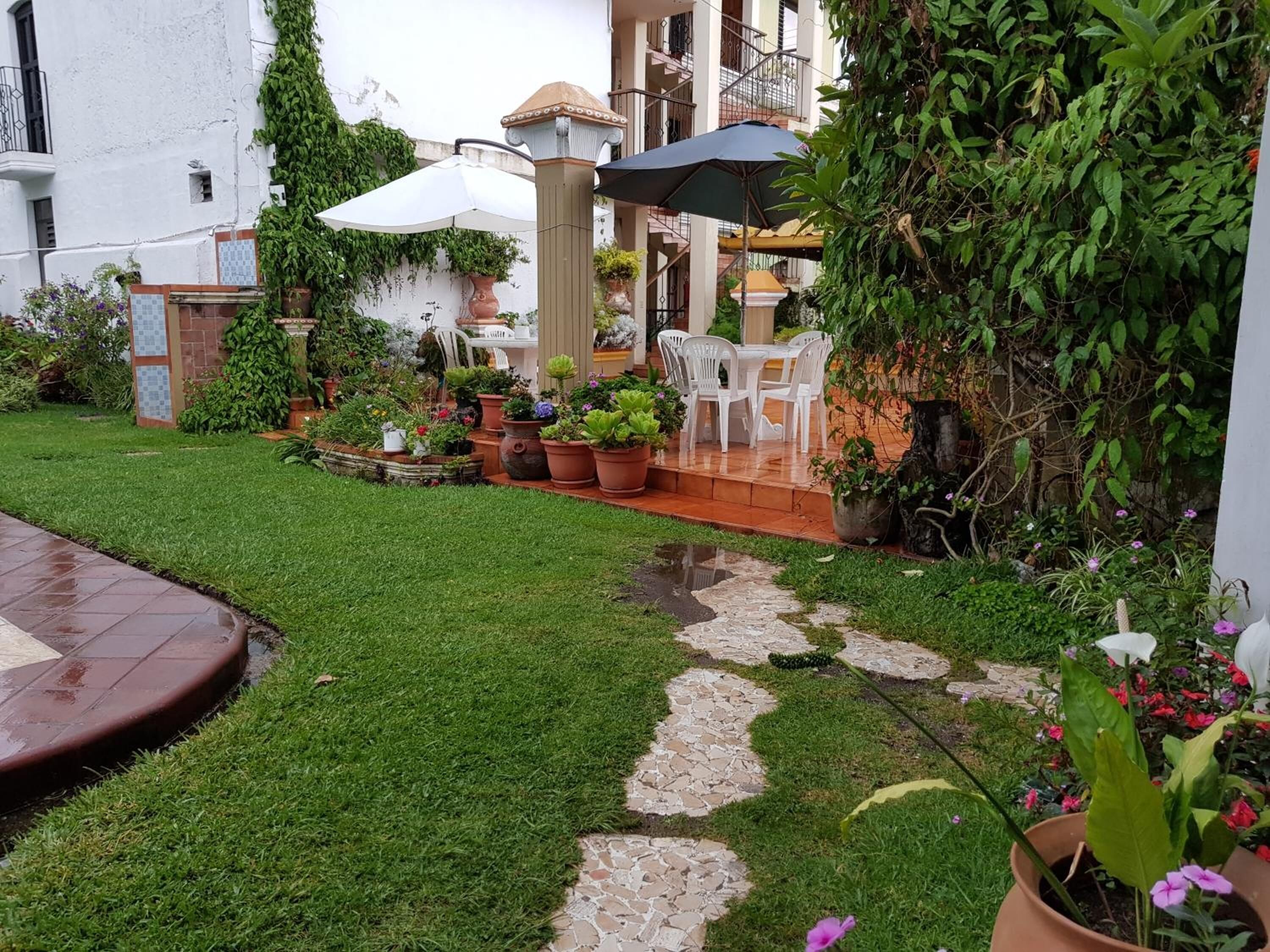 Un jardín bien cuidado con un patio, plantas en macetas y mobiliario exterior.