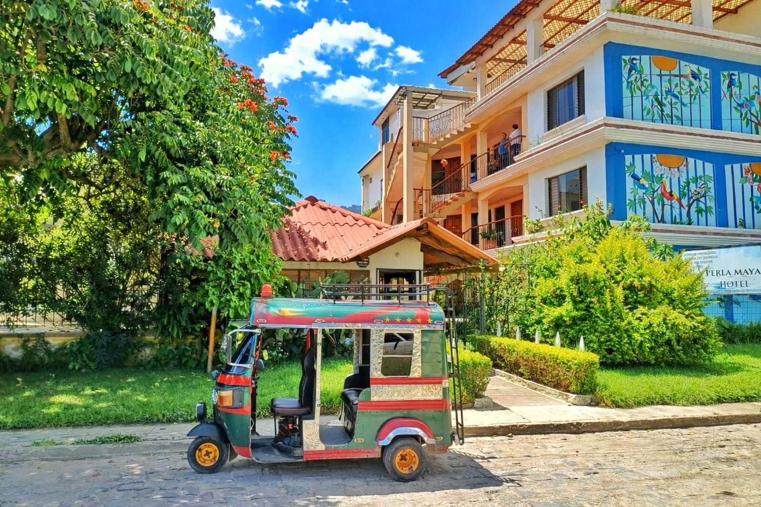 A tuk-tuk parked in front of a hotel with a red roof and a balcony.