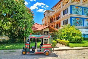 Un tuk-tuk estacionado frente a un hotel con techo rojo y un balcón.
