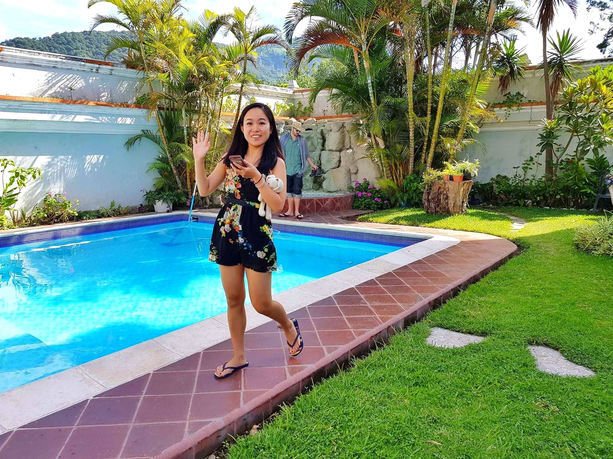 A swimming pool with a tiled edge, surrounded by a grassy area and various plants.