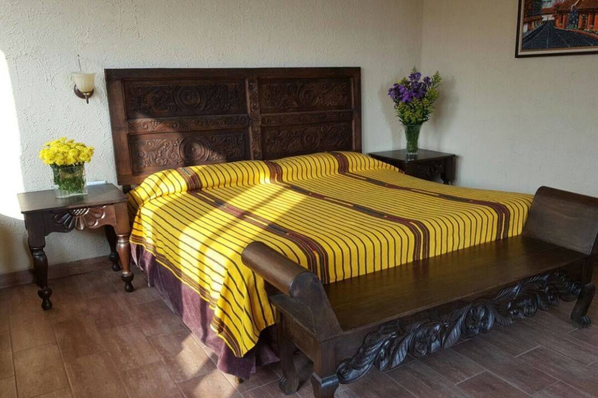 A bedroom with a wooden bed, a nightstand with a vase of flowers, and a framed picture on the wall.