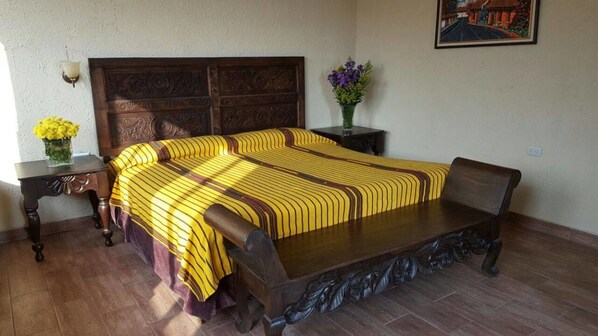 A bedroom with a wooden bed, a nightstand with a vase of flowers, and a framed picture on the wall. - Perla Maya Hotel (Panajachel)