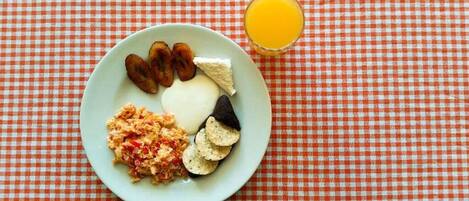 Un plato con huevos revueltos, tostadas, plátanos y un vaso de jugo de naranja sobre un mantel a cuadros.