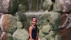 A person in a swimsuit standing in a pool with a rocky waterfall backdrop. - Perla Maya Hotel (Panajachel)
